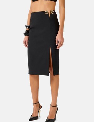 Donna che indossa una gonna a tubino nera a vita alta con spacco frontale e dettagli con fibbia dorata, tacchi neri con cinturino alla caviglia e braccialetti neri.