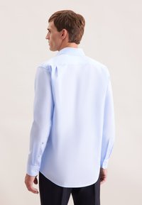 Camicia azzurro chiaro a maniche lunghe con colletto classico, texture liscia, orlo arrotondato e polsini abbottonati. Presenta cuciture sottili sulle spalle.