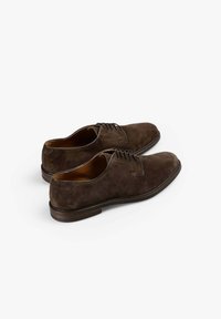 Zapatos de vestir de ante marrón con puntera redonda, cierre con cordones y suela de cuero plana. Los zapatos presentan detalles de costura sutiles.