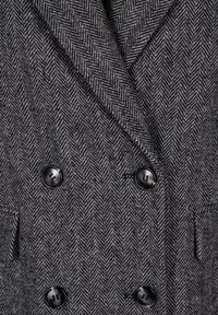 Cappotto grigio a spina di pesce con design doppiopetto, bottoni neri, due tasche laterali e un tessuto testurizzato a contrasto.