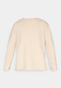 Pull en tricot beige clair avec une coupe ample, des manches longues et un col rond. La texture est côtelée et présente des détails de couture minimaux.