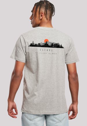 Man with braided hair wearing a gray t-shirt featuring a black mountain and temple skyline with an orange sun and the words "Escape."