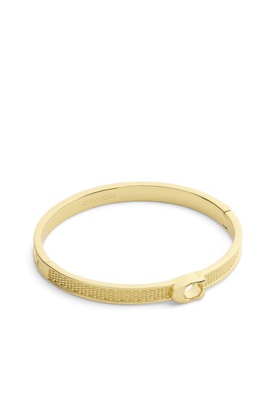 Bracelet jonc Coach ton or avec bande texturée et détail de fermoir sur fond blanc.