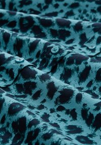 Kurzärmeliges Stoffhemd in Petrol mit schwarzem Tupfenmuster, ausgestattet mit runden Knöpfen und einer glatten Textur.