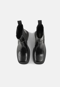 Paire de bottines Chelsea en cuir noir à bout carré, panneaux latéraux élastiques et languettes, vues de dessus sur un fond uni clair.