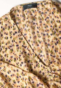 Blusa de estampado animal con diseño de escote en V en color beige, que presenta un patrón de manchas marrones, verdes y moradas, fabricada con tejido ligero.