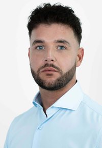 Lichtblauw overhemd met knopen en een kraag, gemaakt van zacht materiaal en met een getailleerd ontwerp. Het model heeft kort donker haar en een verzorgd baardje.