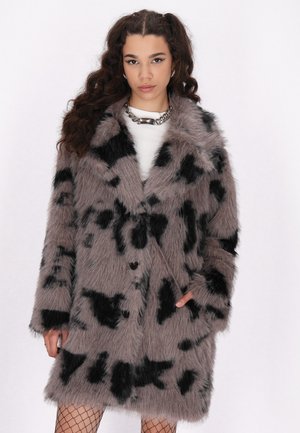 Cappotto in pelliccia sintetica grigia con macchie astratte nere, design doppiopetto, colletto a rever e tasche laterali. Il modello indossa leggings a rete e accessori argentati.