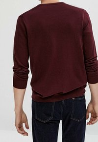 Bordeaux crew-neck sweater met lange mouwen, geribbelde manchetten en zoom. Gedragen over donkerblauwe spijkerbroeken, met een gladde gebreide textuur.