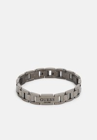 Bracciale in metallo con finitura gunmetal lucida, caratterizzato da maglie rettangolari, tre accenti in cristallo trasparente e un logo inciso centrale.