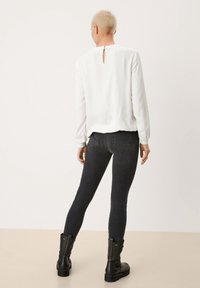 Blusa blanca de manga larga con un agujero en la espalda y jeans negros ajustados. El conjunto se complementa con botas negras de tobillo. Acabado de tejido suave.