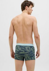Boxeri dintr-un material elastic cu un model de camuflaj verde, având o curea elastică de culoare albastru deschis pe care este inscripționat numele brandului.