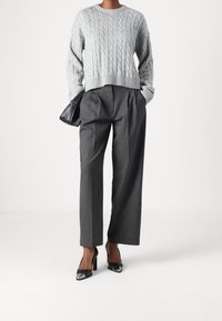 Pull gris à maille torsadée avec bords côtelés, assorti à un pantalon taille haute à fines rayures et des escarpins en cuir verni noir. Sac à main noir.