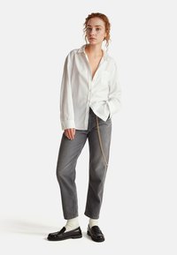 Camicia bianca con bottoni e maniche lunghe, abbinata a jeans grigi. Dettaglio a catena sui pantaloni, abbinati a mocassini neri e calzini bianchi.