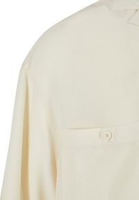 Chemise beige en tissu lisse, dotée d'une poche poitrine et d'une fermeture à boutons. Design simple et décontracté avec une texture douce.