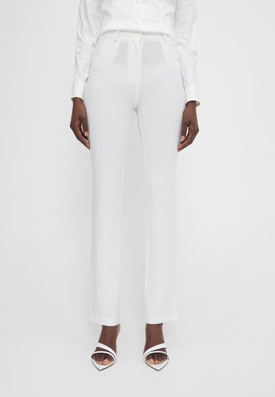 Pantalones cortos blancos de tela suave, con una cinturilla plana, bolsillos laterales y un corte recto. Combinados con tacones abiertos blancos.