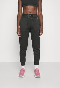 Černé joggingové kalhoty s elastickým pasem, šňůrkou a manžetami na spodním okraji. Obsahují boční kapsy a logo na levém stehně.