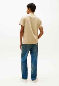 T-shirt in cotone beige a maniche corte, con scollatura rotonda, abbinato a jeans blu in denim e scarpe da ginnastica bianche.
