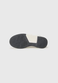 Sål med to-farget design, som har en svart teksturert gummidel og en beige mønstrete gummidel for bedre grep.