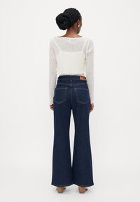 High-waisted dark blue wide-leg jeans with a tan leather tag on the back. The cropped light sweater has a textured finish and scalloped hem.