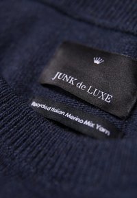 Marinefarbener Strickpulli mit einem "JUNK de LUXE"-Markenschild und einem zweiten Schild, das Recyclinggarn aus italienischer Merinowolle mischt.