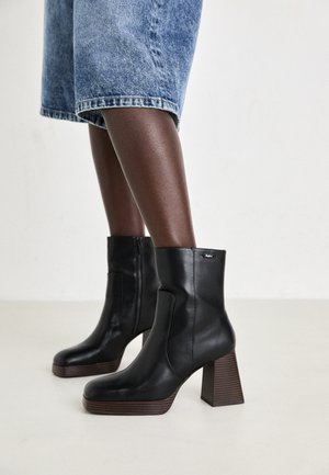 Melni ādas potīšu zābaki ar masīlu, struktūrētu koka papēdi un sānu rāvējslēdzēju. Dizainam ir gluda apdare un pieguļoša potītes forma.