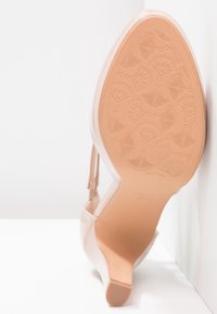 Chaussure à talon haut couleur nude avec une finition brillante, dotée d'un bout pointu et d'un talon fin texturé. La semelle présente un motif floral.