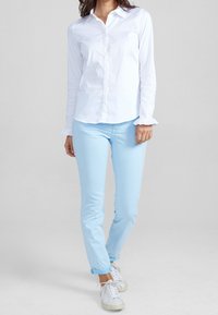 Camicia bianca con maniche a ruffle, abbinata a pantaloni su misura azzurri e sneakers bianche con lacci e suole strutturate.