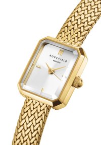 Montre rectangulaire dorée avec un bracelet en maille texturé, un cadran blanc texturé, des aiguilles dorées et une lunette hexagonale. Nom de la marque "ROSEFIELD" affiché.