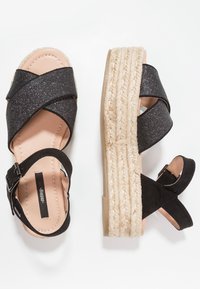 Czarnie espadryle na platformie z krzyżującym się wzorem, błyszczącymi paskami, regulowanym zapięciem w kostce oraz plecioną, jutową podeszwą.