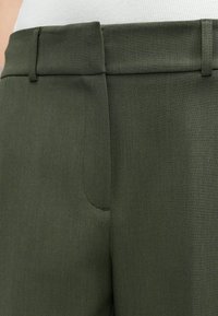 Spodnie w oliwkowej zieleni o dopasowanym kroju, z płaskim przodem, szlufkami na pasek i boczną kieszenią. Tkanina jest gładka z subtelną fakturą.