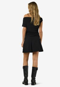 Črna off-shoulder majica je kombinirana s črno plisirano krilo, nošena z visokimi črnimi usnjenimi čevlji z zaponkami. Gladek, teksturiran material.