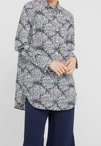 Camicia a bottoni floreale in navy e bianco, con colletto alla francese, maniche lunghe, orlo leggermente curvo e vestibilità ampia con intricate decorazioni a foglia.