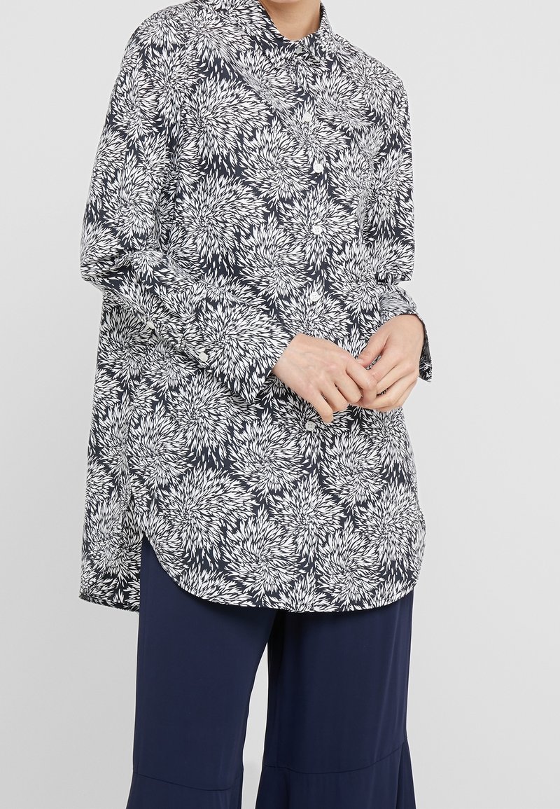 Camicia a bottoni floreale in navy e bianco, con colletto alla francese, maniche lunghe, orlo leggermente curvo e vestibilità ampia con intricate decorazioni a foglia.