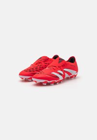 Red soccer cleats with a textured upper, featuring black accents and three white stripes, designed for traction with molded studs.