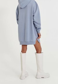 Robe sweat à capuche bleu clair surdimensionnée avec une capuche, des fentes latérales et des poignets côtelés, assortie à des bottes blanches à plateforme montant jusqu'aux genoux.