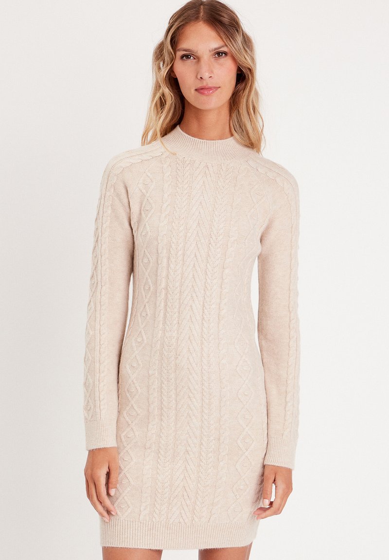 Robe en tricot beige clair avec un col haut, des manches longues et des motifs en câble texturés sur l'ensemble. Tissu doux et léger.
