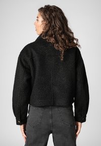 Black cropped jacket made from textured material with a slightly oversized fit, featuring a large collar and buttoned cuffs.