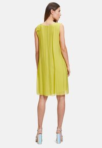 Ärmelloses, limegrünes Chiffonkleid mit fließender Form, das an der Schulter mit einer kleinen Schleifenakzentuierung verziert ist und einen Saum hat, der bis zur Mitte des Oberschenkels reicht.