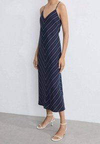 Námořnické midi šaty s bílými vertikálními pruhy, tenkými ramínky a v-výstřihem. V kombinaci s bílými sandály na podpatku.