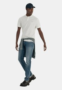 Maglietta bianca a maniche corte con colletto a bottoni, maglione grigio annodato in vita, jeans blu e sneaker nere chunky.