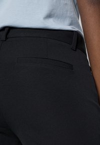 Pantalon noir à texture lisse et coupe ajustée. Dispose d'une petite poche arrière avec une ceinture propre et minimaliste.