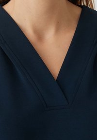 Top blu navy con scollo a V, realizzato in tessuto morbido; presenta cuciture dettagliate lungo il collo e le spalle.