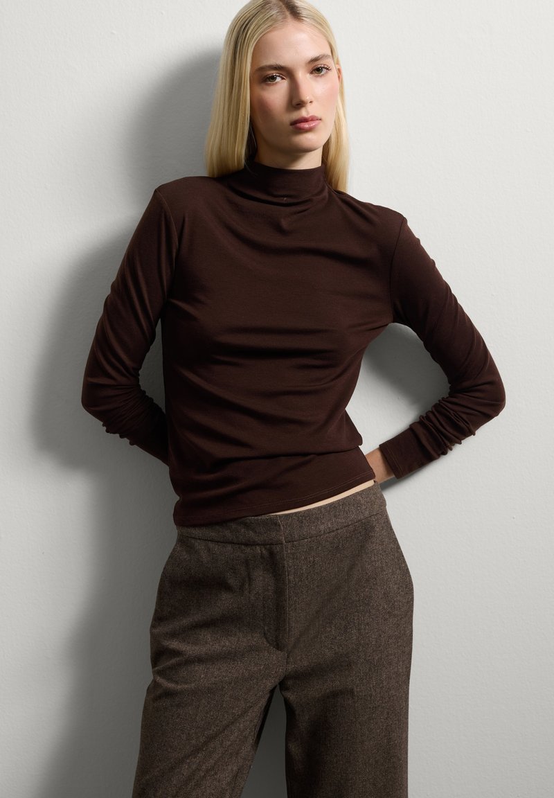 Bruine lange mouwen turtleneck top van een gladde stof, gecombineerd met bruine gestructureerde broeken met een rechte snit en steekzakken.
