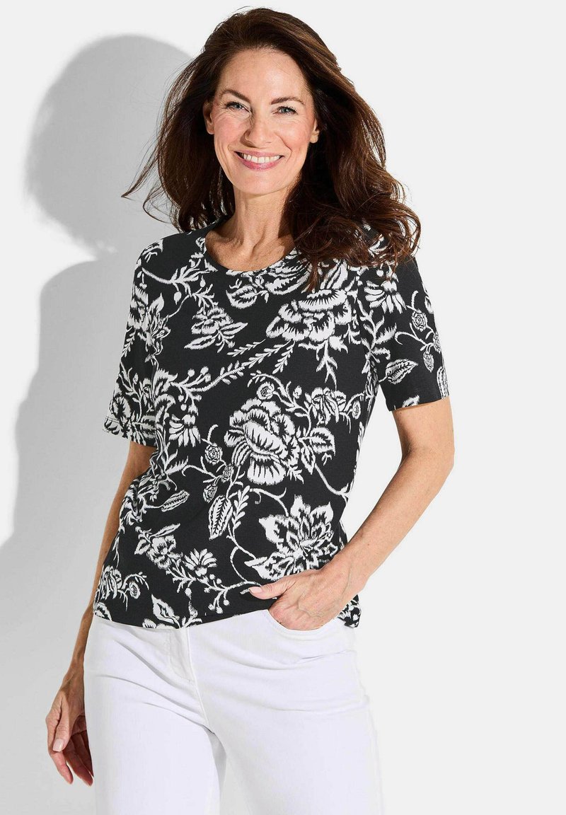 Zwart shirt met korte mouwen, voorzien van een wit bloemenpatroon, een ronde halslijn en een relaxed fit, gecombineerd met witte broek.