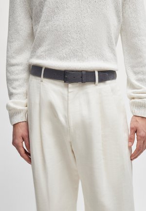 Grijze suède riem met een rechthoekige zwarte metalen gesp, gedragen over lichtbeige linnen broek, gecombineerd met een witte gebreide textuurtrui.