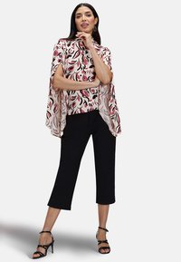 Flödande rosa och krämfärgad blus med abstrakt mönster i svart och röd, kombinerad med svarta cropped byxor och strappy svarta klackar.