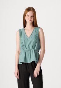 Svetlá tyrkysová bezrukávová blúzka s výstrihom do V, čipkovým lemom na pleciach a naťahovaným peplum lemom. Tkanina má jemnú štruktúru.