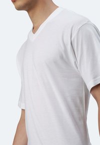 T-shirt bianco a V con maniche corte, realizzato in morbido cotone, dal texture liscia e dalla vestibilità aderente. Nessun motivo o accento visibili.