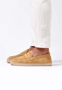 Mocasines de ante en tono marrón claro con un acabado texturizado, que presentan un lazo decorativo, costuras en contraste y una suela de yute trenzado. Talla estándar.